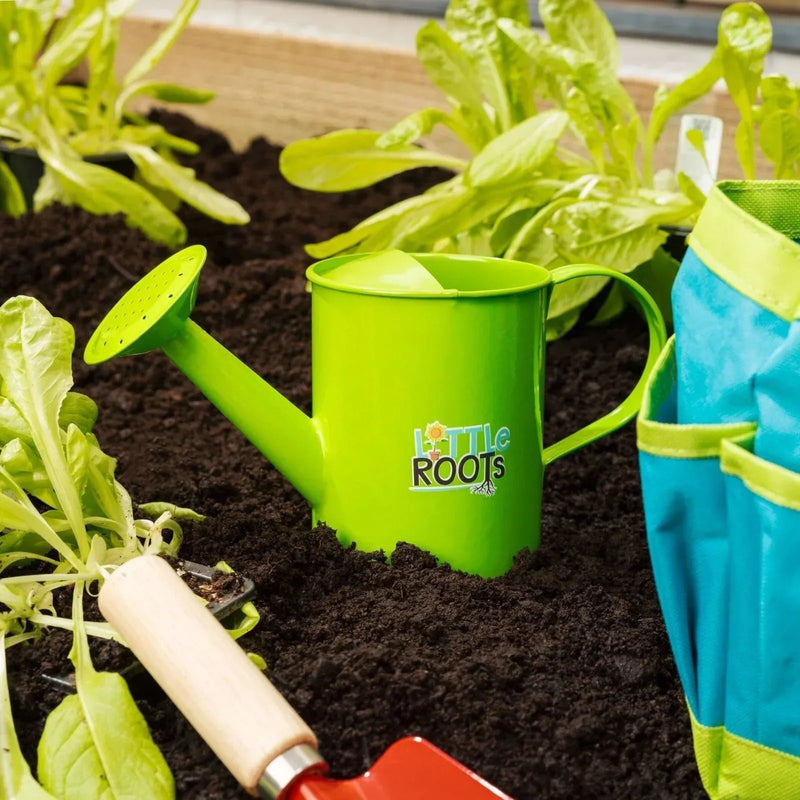 Little Roots tool bag beside a green watering can and garden tools in soil