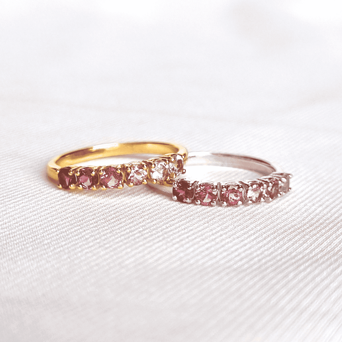 Two eternity bands with pink and clear stones; one gold-toned, one silver-toned