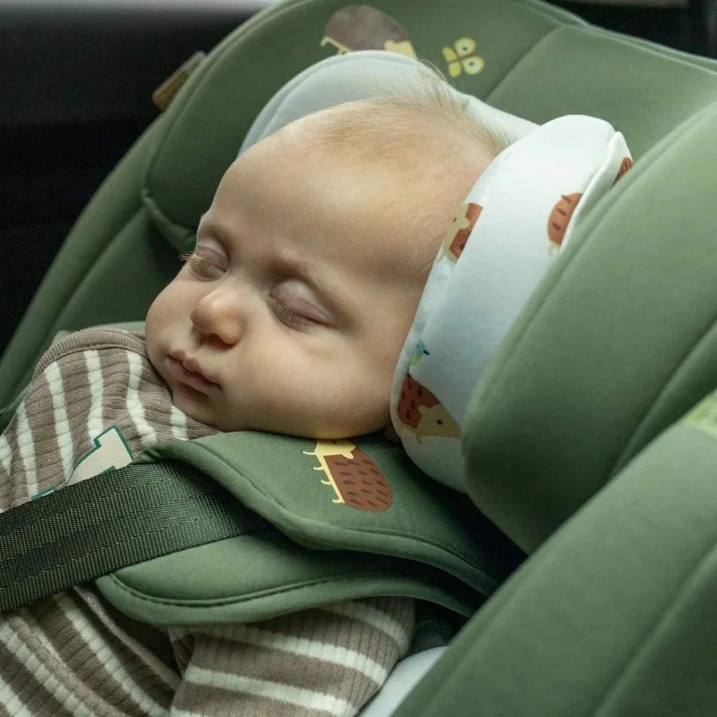 Sleeping baby in green car seat with cushioned head support and harness.