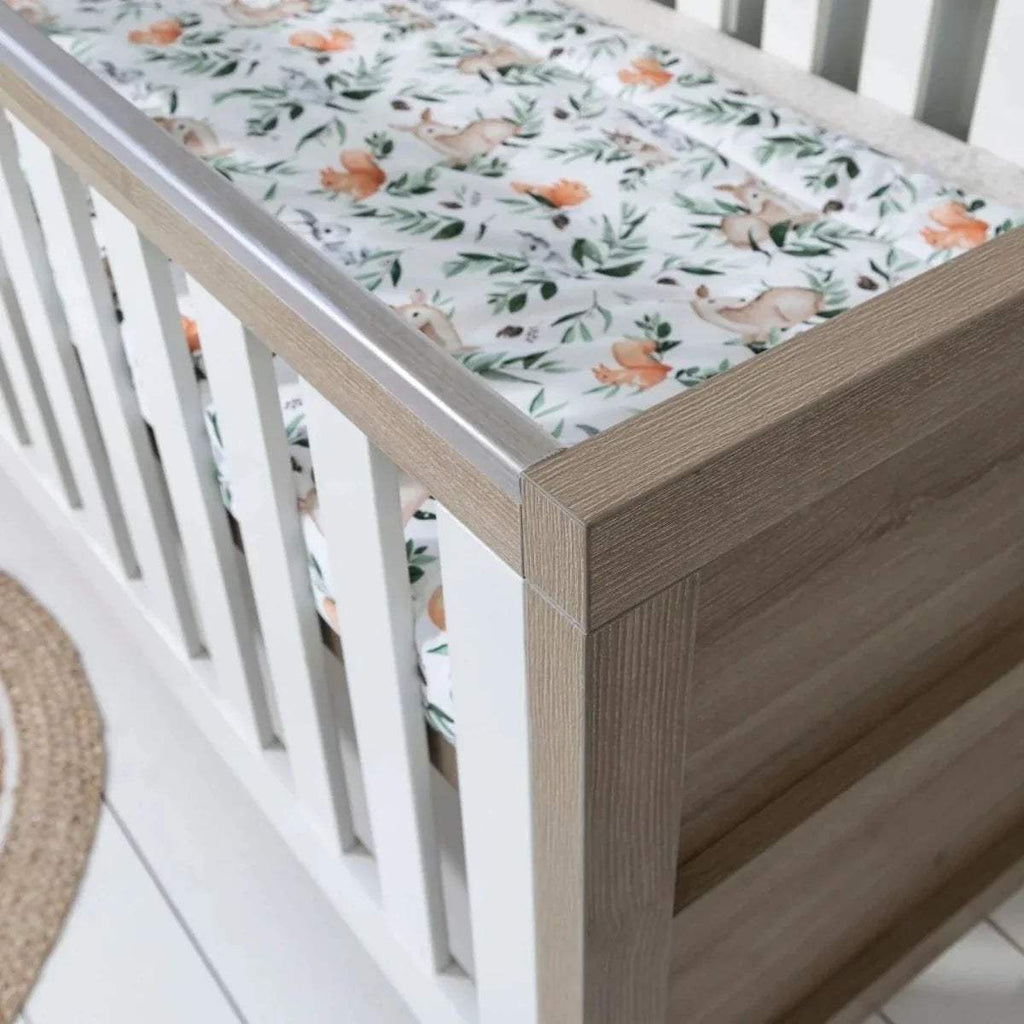 Oak bed corner with vertical slats and floral bedding on mattress