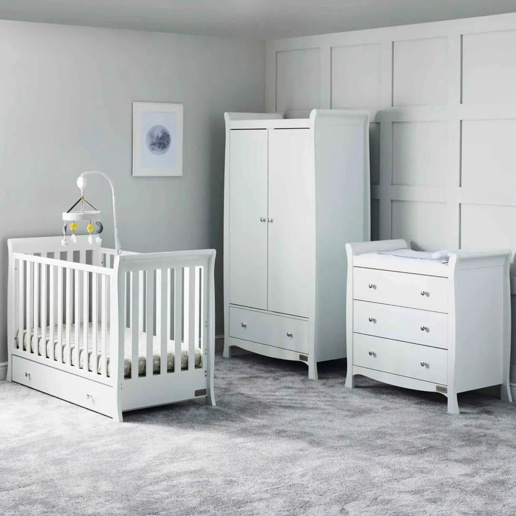 White mini cot bed with drawer base, wardrobe, and matching dresser in a nursery room