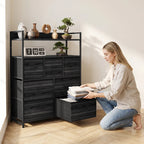 Black wood-effect dresser with open shelves and seven drawers, person loading linens