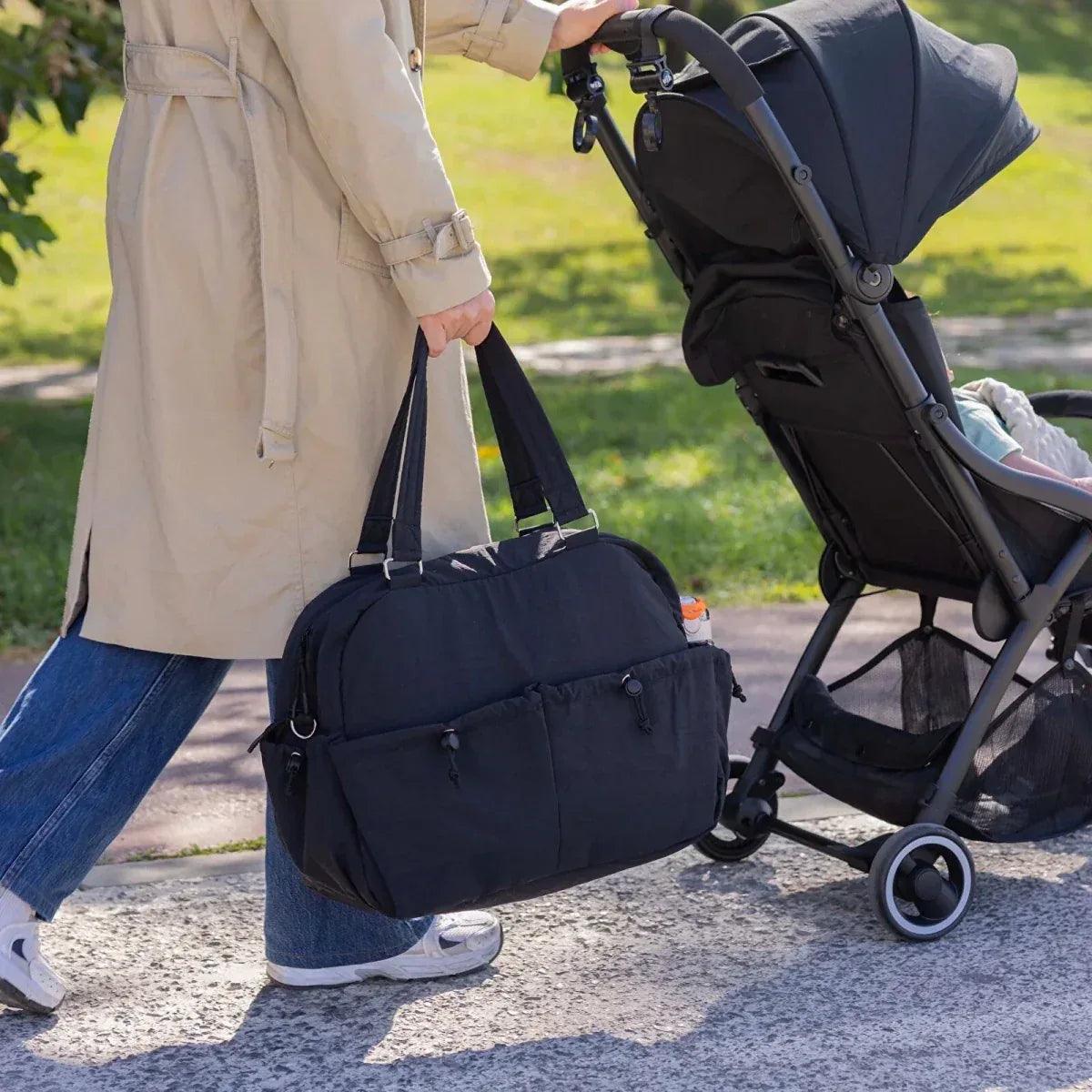Black quilted shoulder bag carried by an adult near a stroller