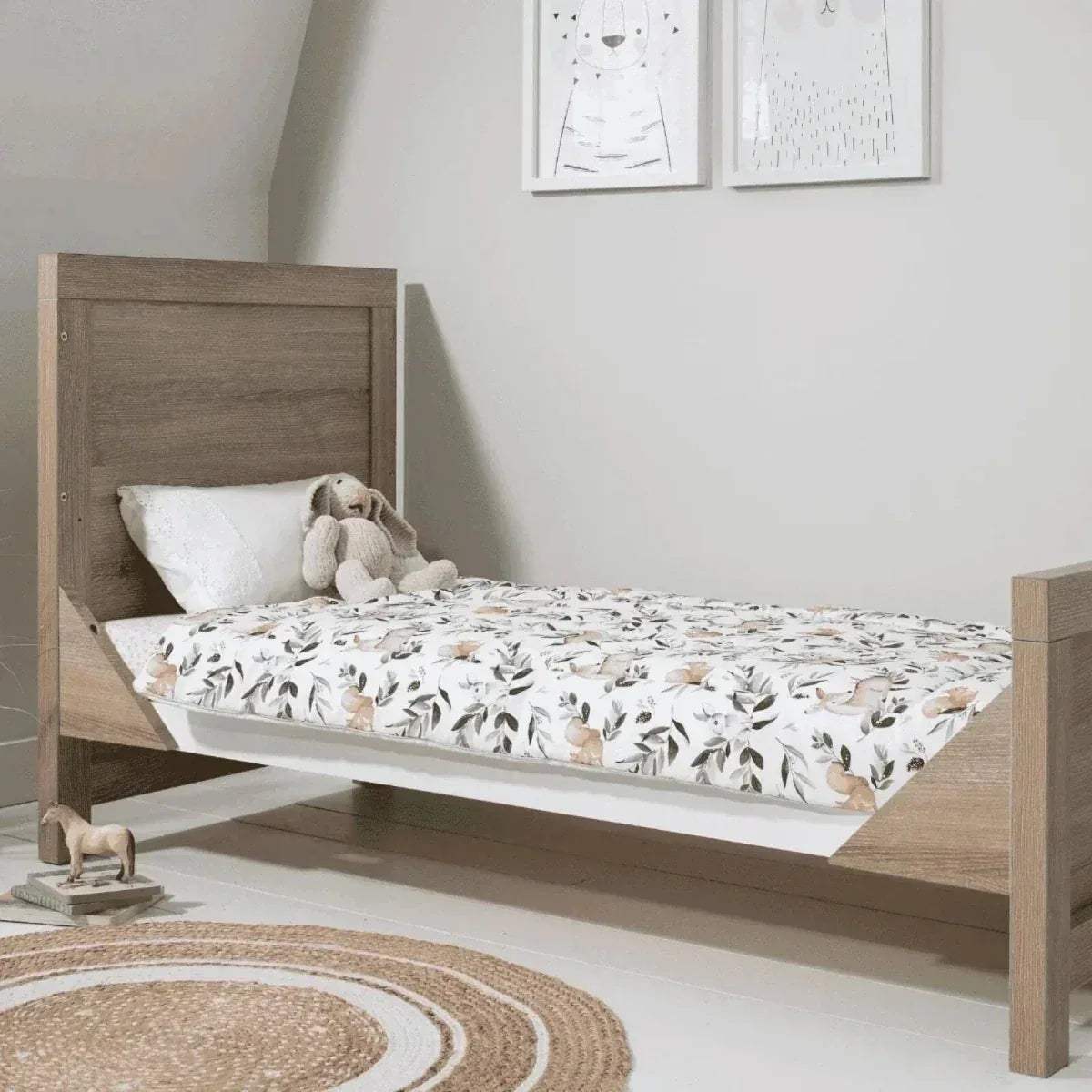 Oak and white cot bed with leaf-pattern bedding and pillows
