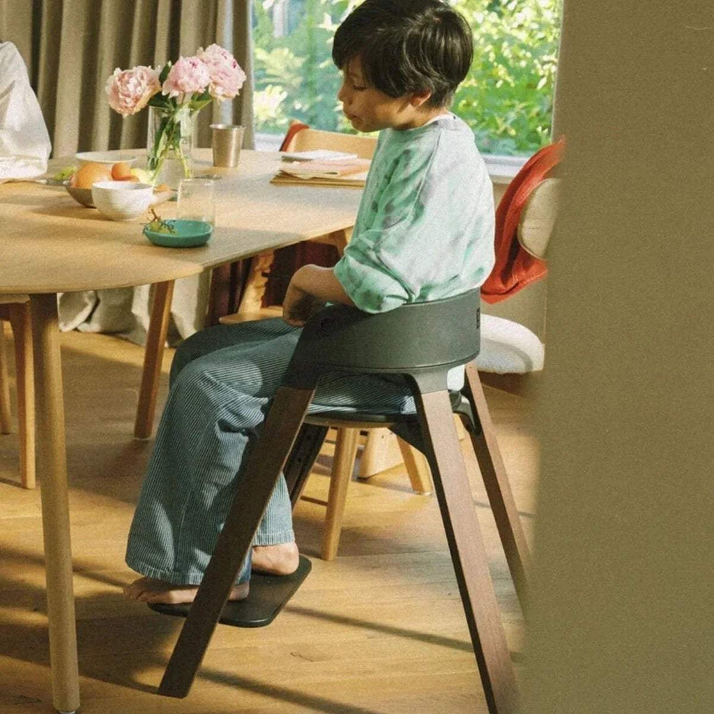 Black highchair with child sitting at a table; warm brown legs and rounded back