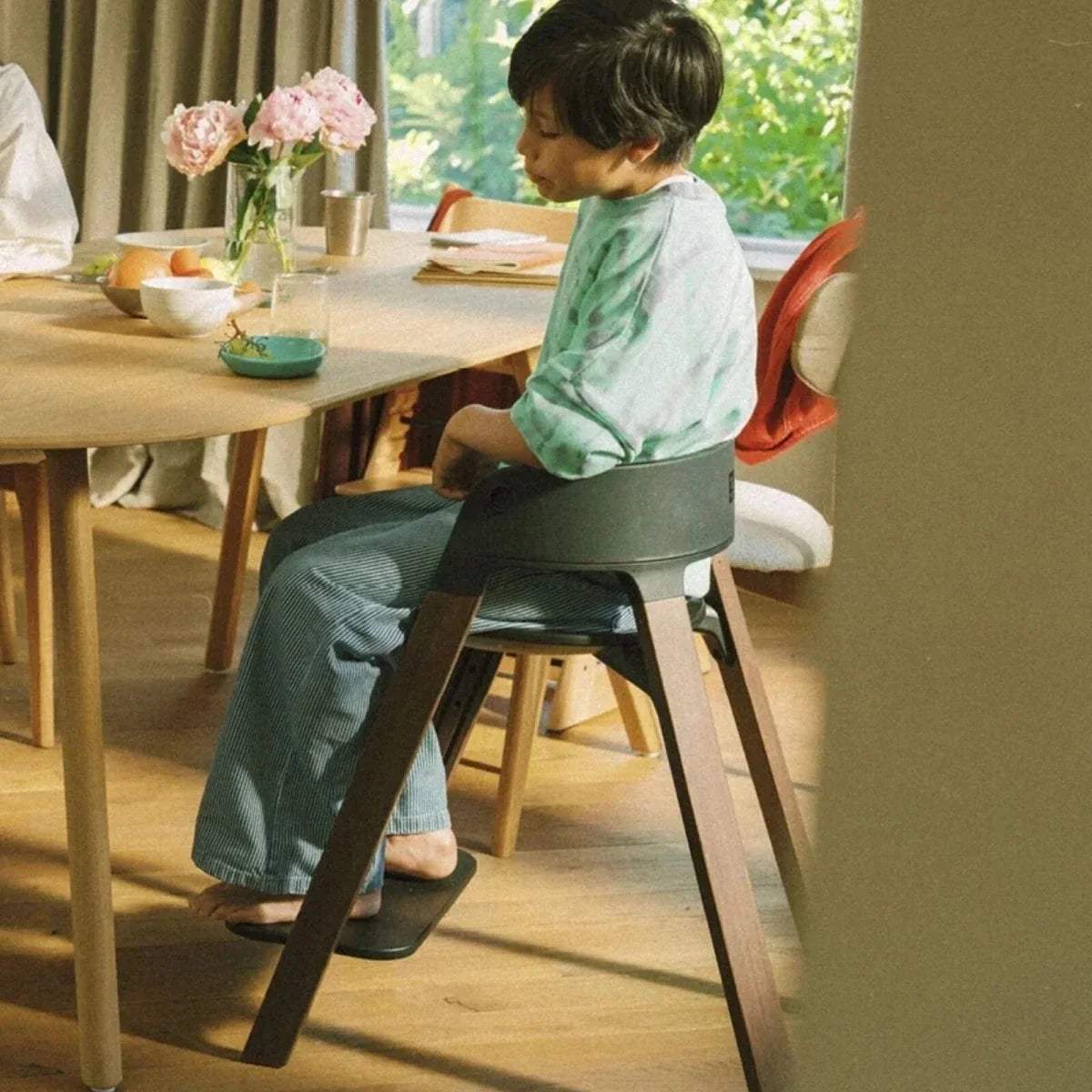 Black highchair with child sitting at a table; warm brown legs and rounded back