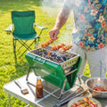 Green portable charcoal BBQ grill with food on wire grate and side handles
