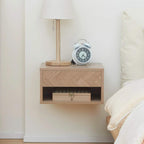 Natural wood floating bedside table with drawer and open shelf beside bed.