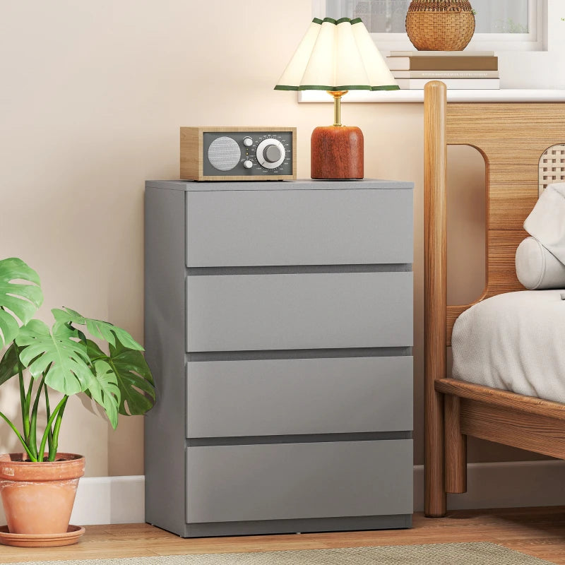 Grey four-drawer chest dresser with recessed drawer fronts beside bed and decor.