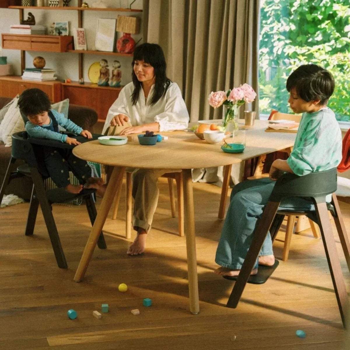 Stokke Steps highchair with dark seat and tray, child seated at a wooden table