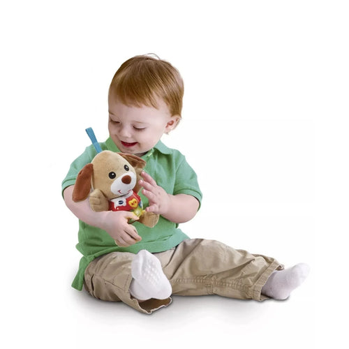 Puppy plush held by child: brown ears, cream face, red activity shirt