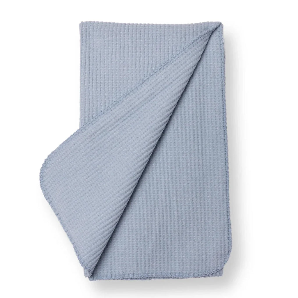 Blue waffle-knit baby blanket folded with one corner draped over the edge