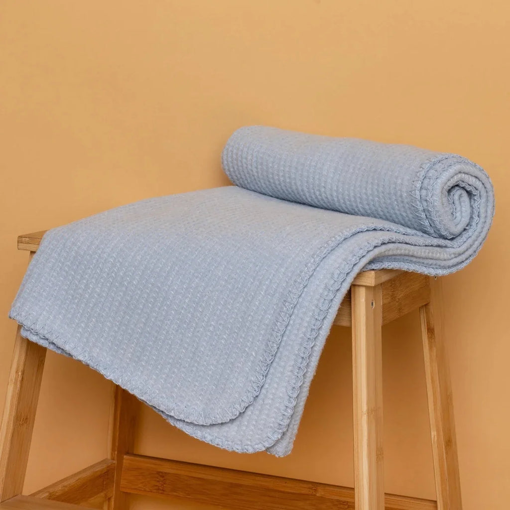 Blue waffle-knit baby blanket rolled on a small wooden step stool