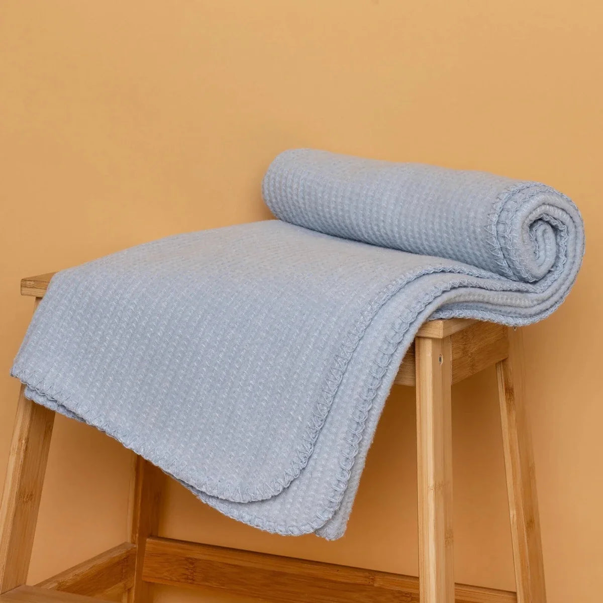 Blue waffle-knit baby blanket rolled on a small wooden step stool