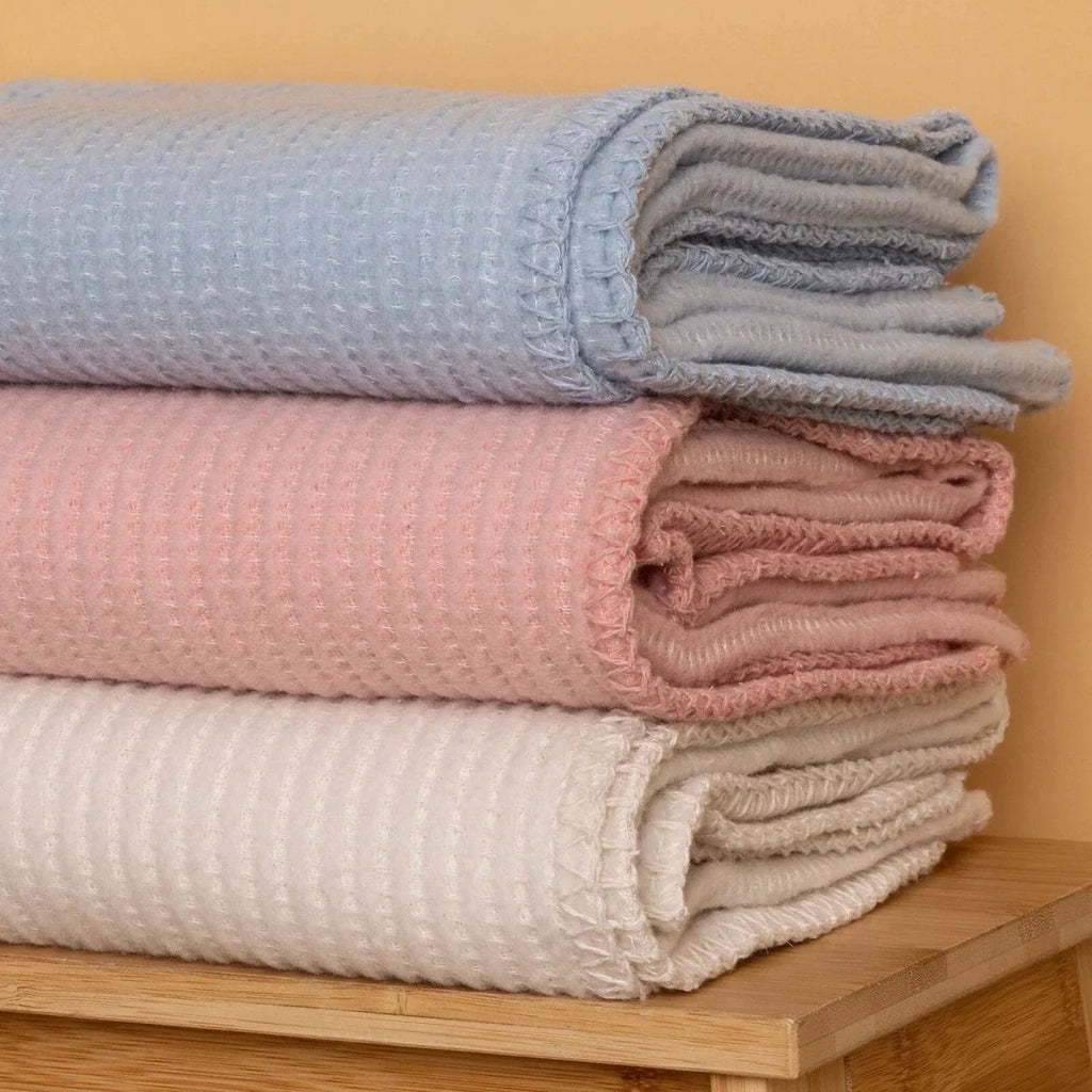 Stack of folded baby blankets in blue, pink, and beige on a wooden shelf