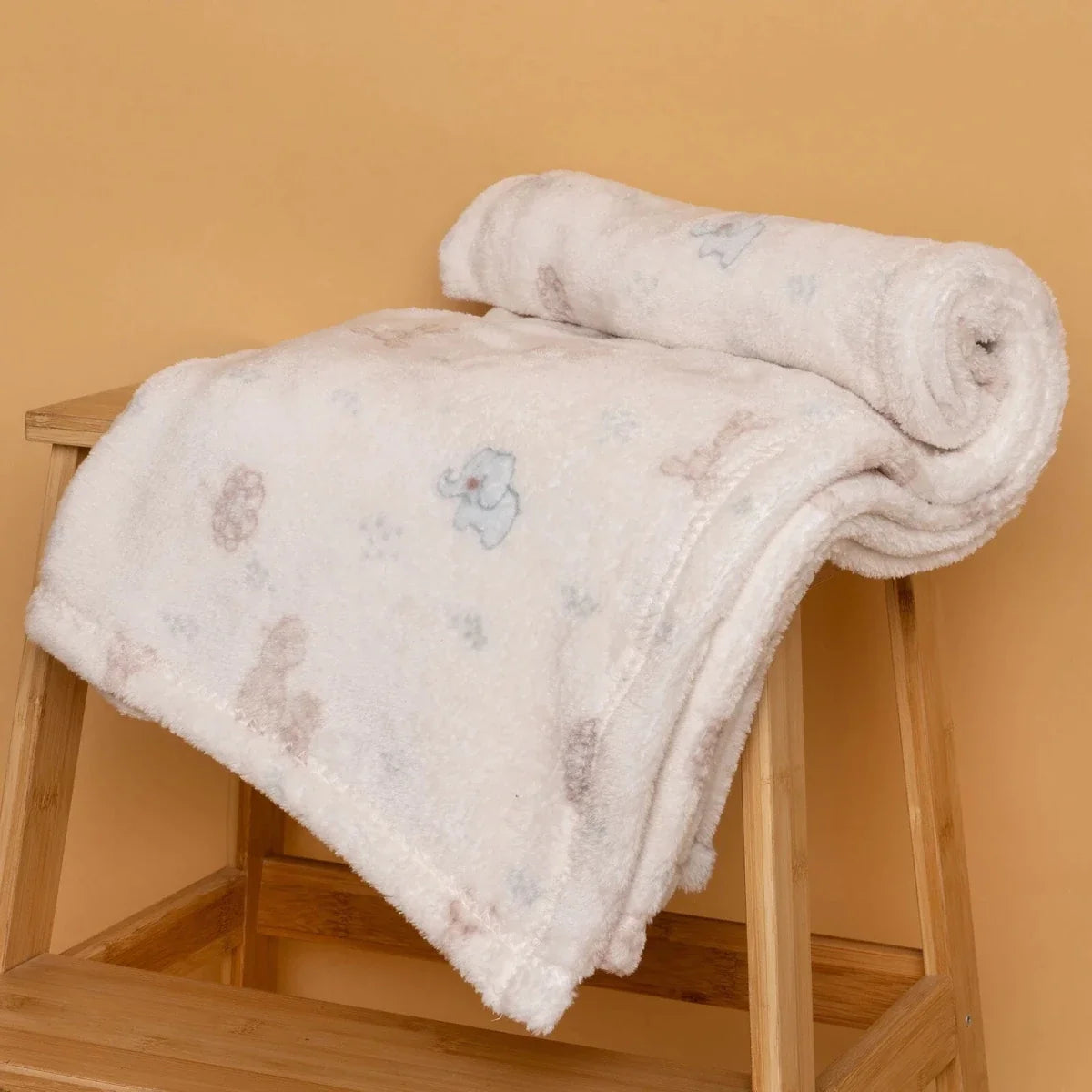 Light cream animal-print fleece baby blanket draped over a wooden chair