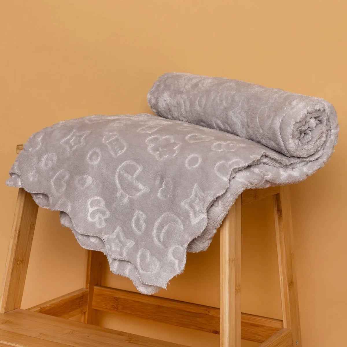Grey baby blanket folded over wooden chair with sky-themed icons on fleece