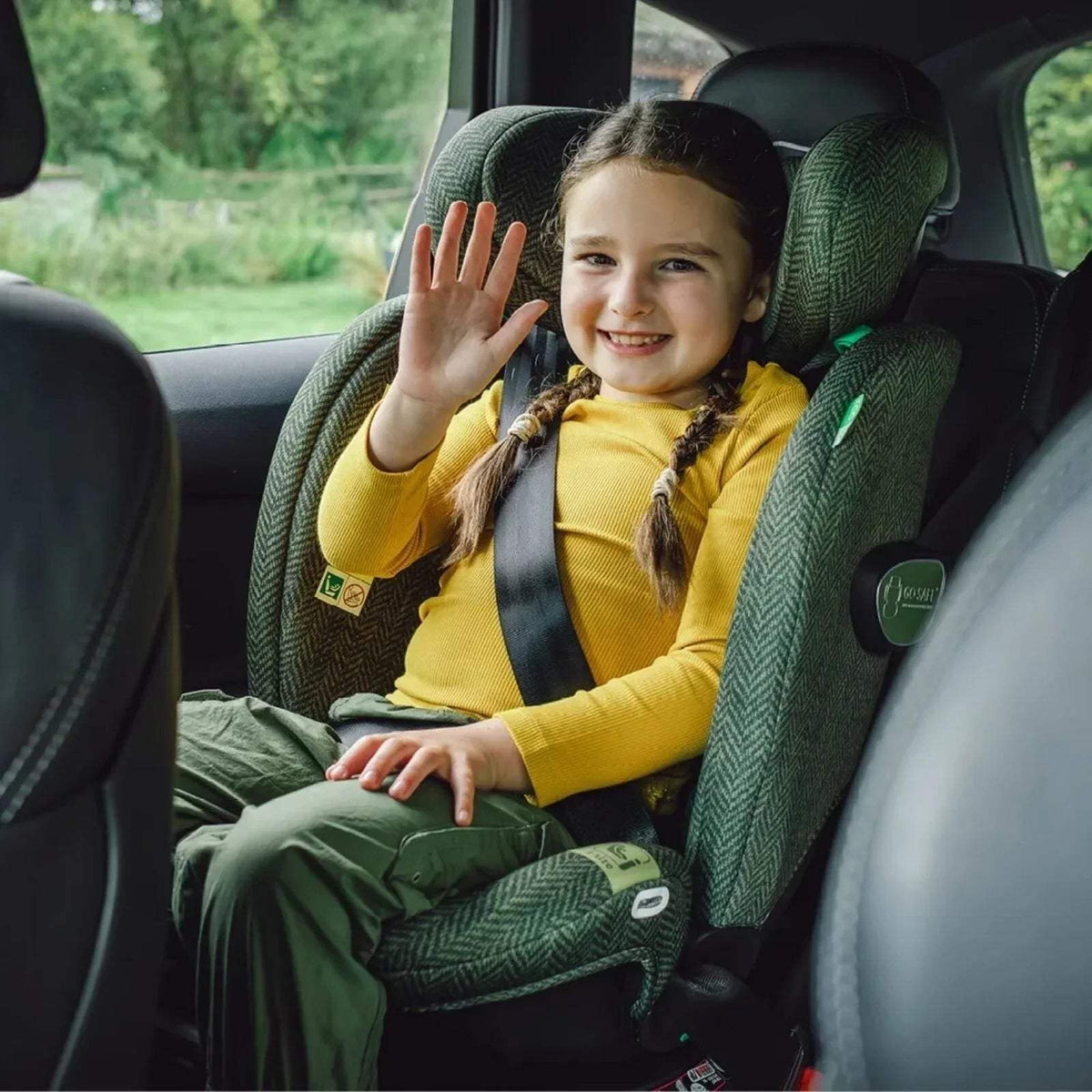 Green tweed car seat with side wings and padded harness, child seated