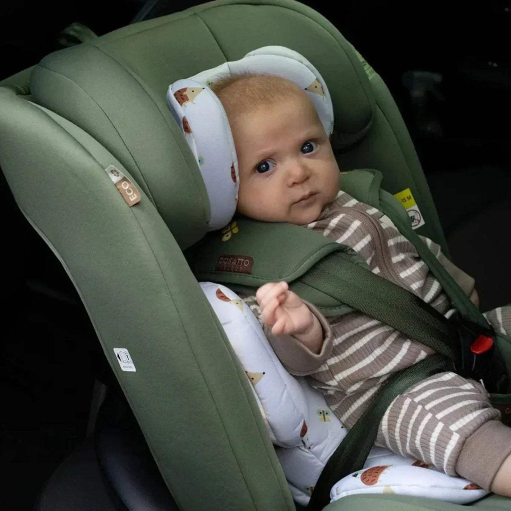 Infant in green child car seat with cushioned head support and safety harness.