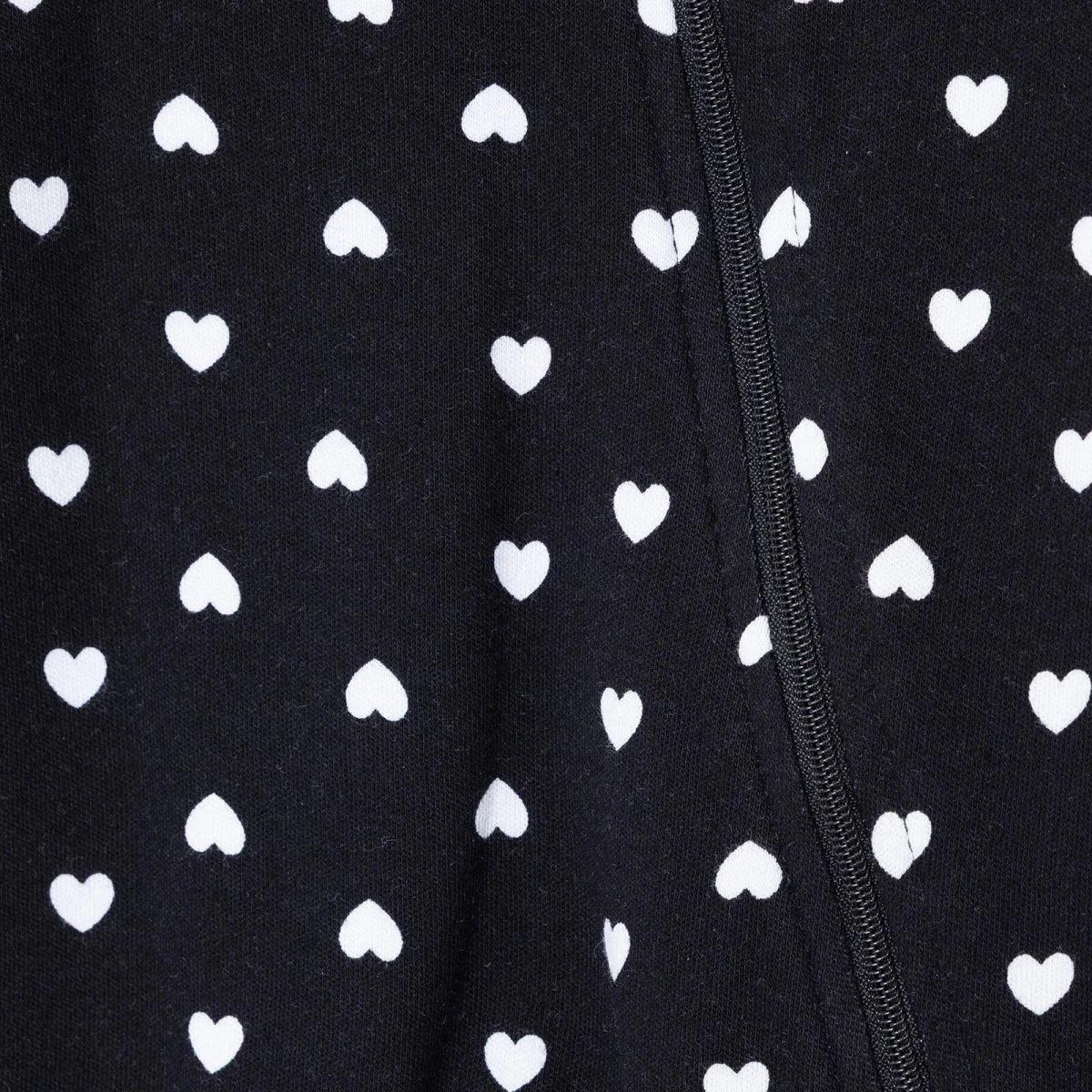 Black fabric close-up of heart print on long-sleeve baby sleepsuit, zipper edge