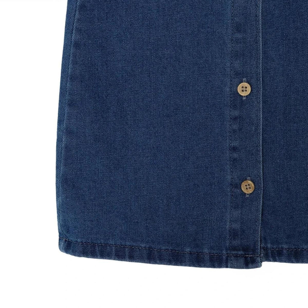 Indigo denim pinafore dress lower front hem with subtle stitching and panel seams