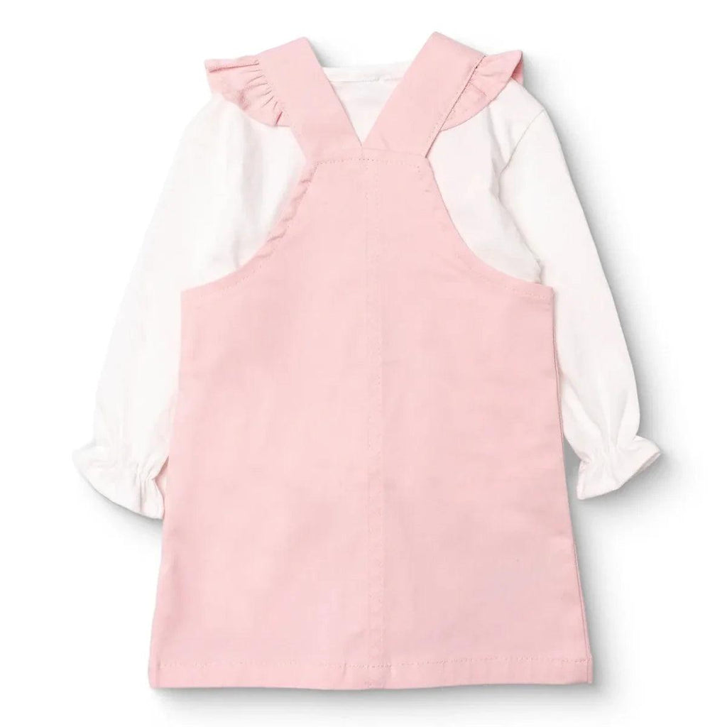 Pink sleeveless dungarees dress with two buttons, worn over white long-sleeve top