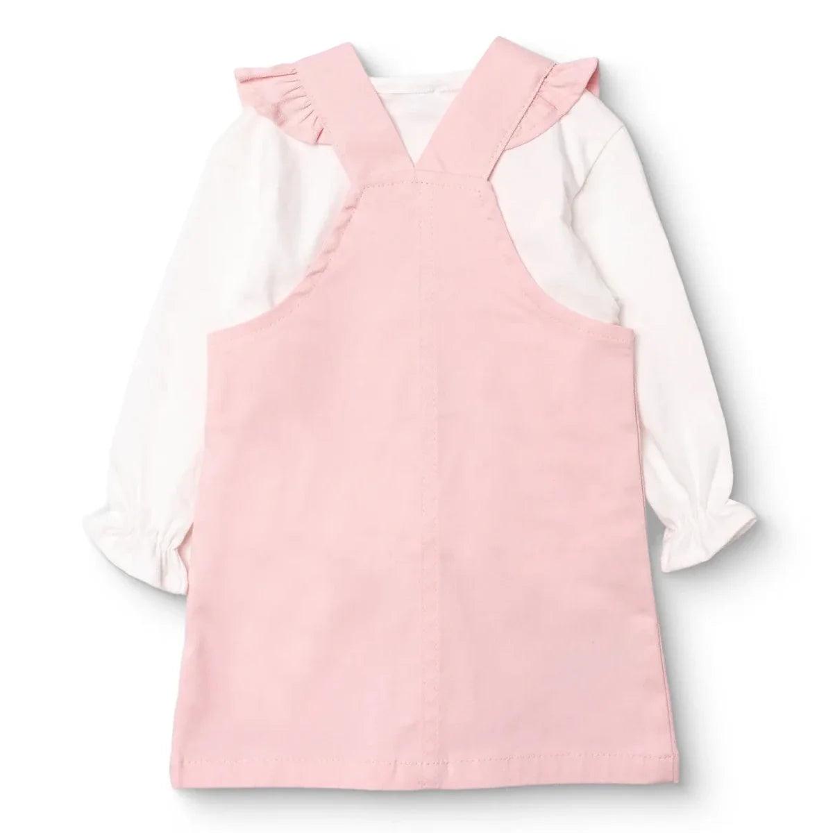 Pink sleeveless dungarees dress with two buttons, worn over white long-sleeve top