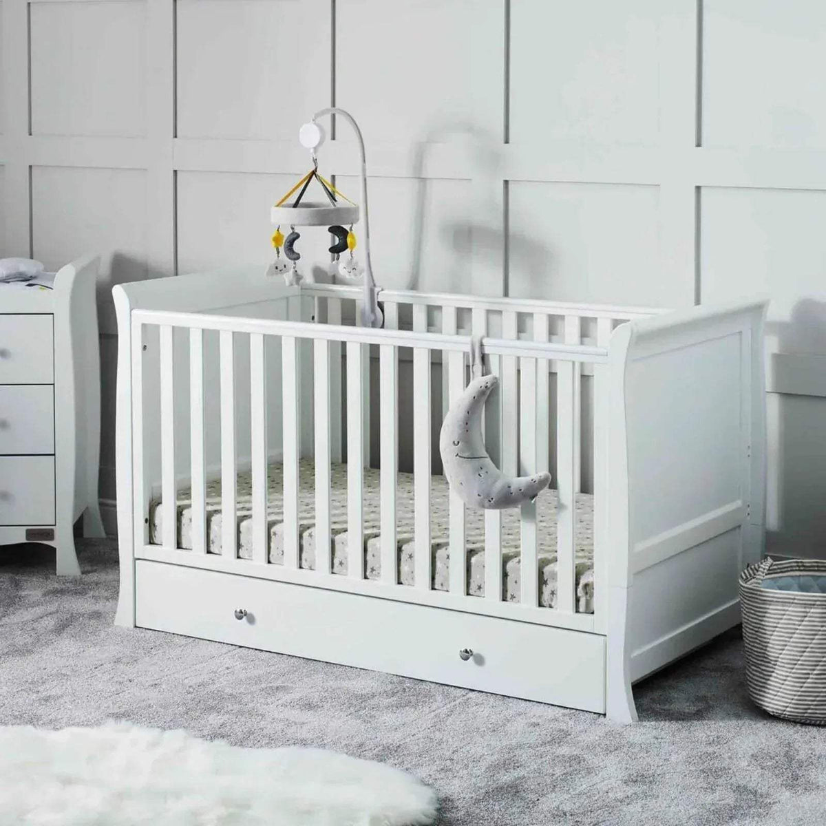 White cot bed with raised sides and slatted headboard, drawer base with bedding set.