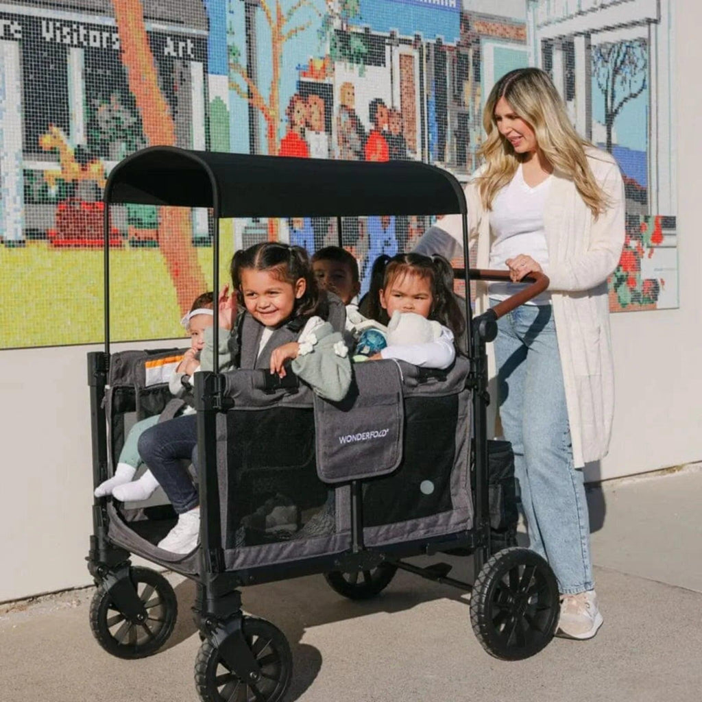 Jet black stroller wagon with canopy, standing family with children in the seats outdoors