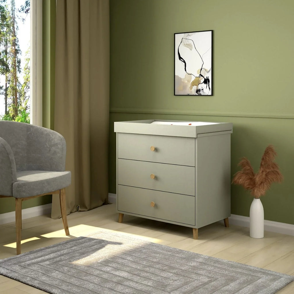 Grey kids changing dresser with three drawers and gold knobs, shown in a room setting