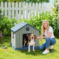 Grey outdoor dog house with blue roof and paw-print front panel; dog standing in yard