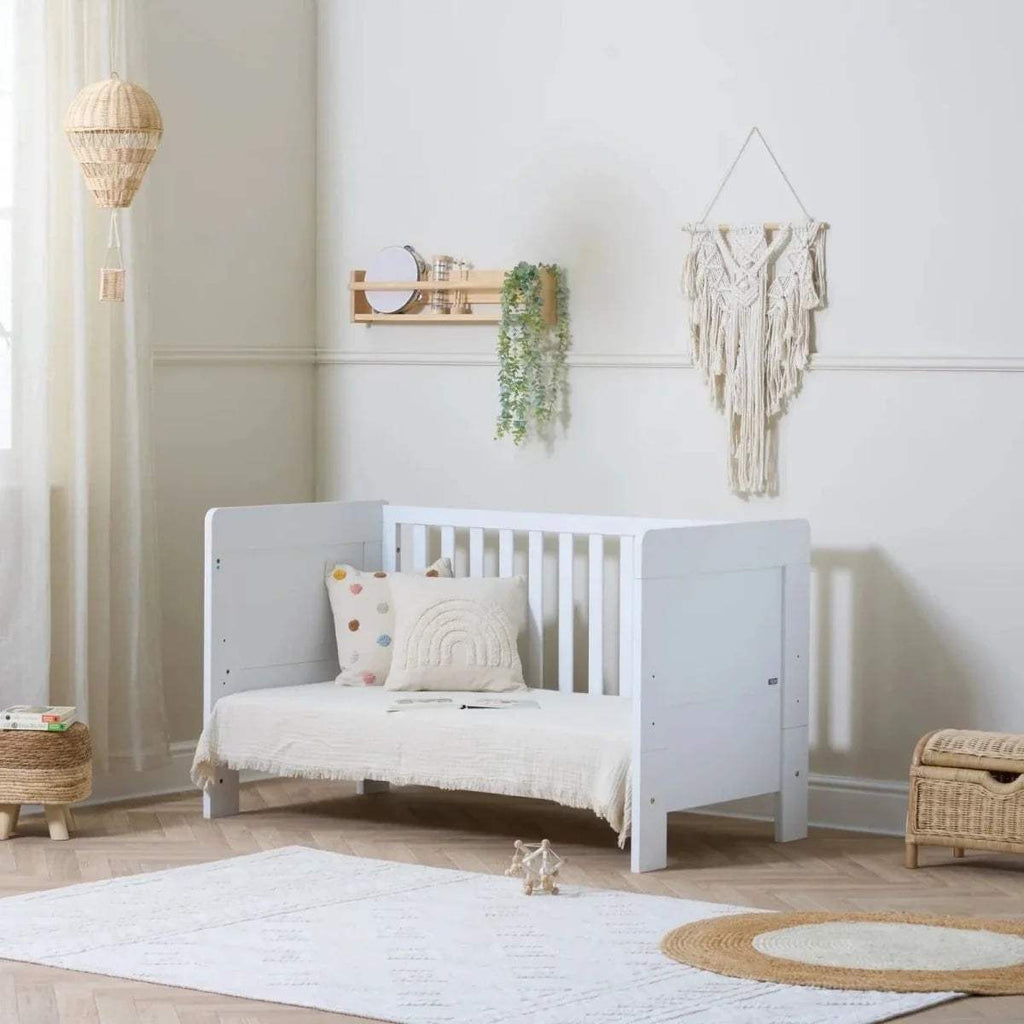 White cot bed with vertical slat rail, protective side rails, and raised headboard