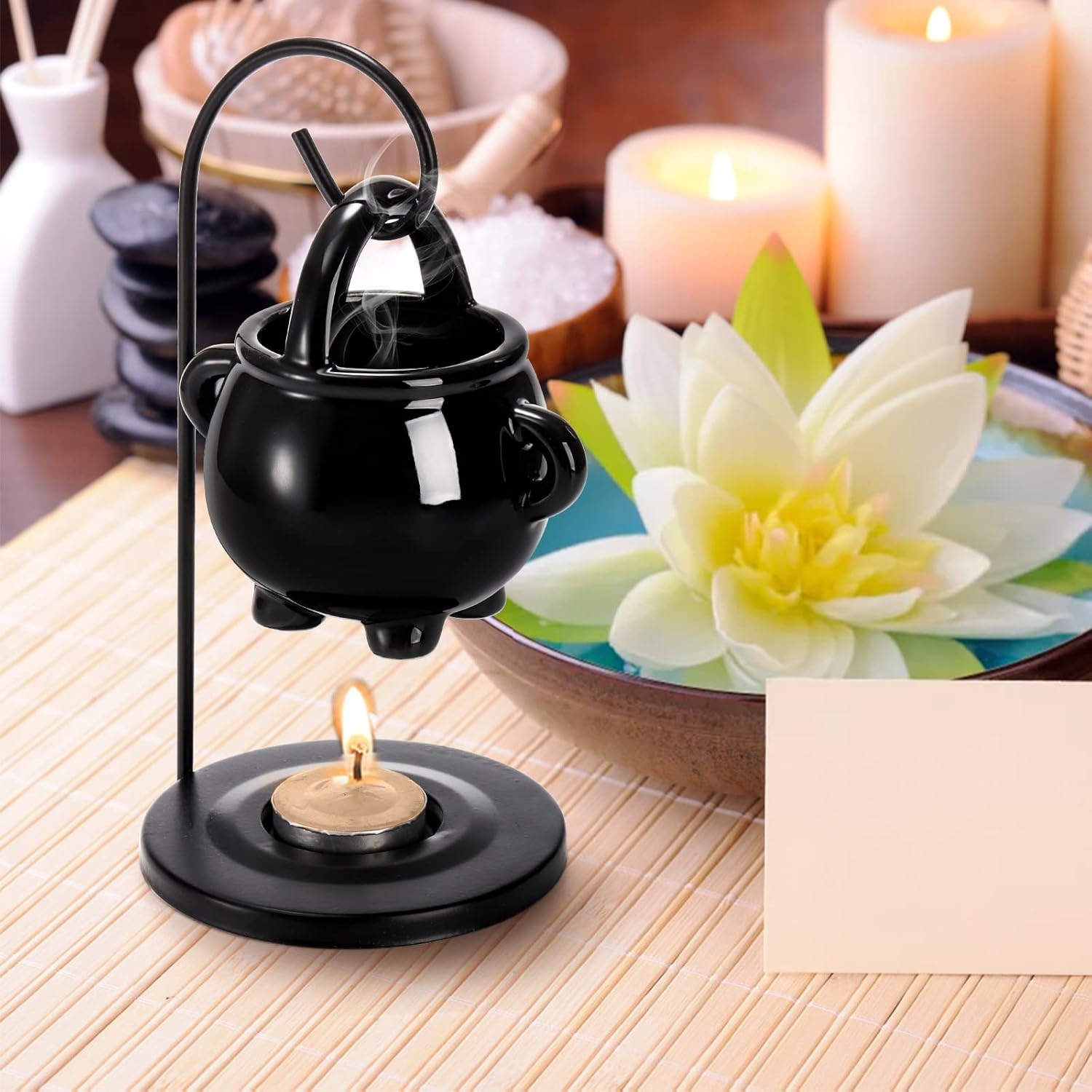 Black incense burner on a wooden surface with candles and a flower in the background