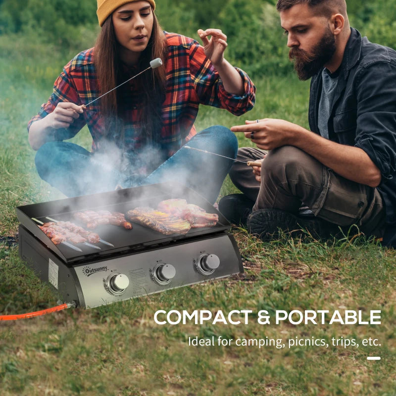 Portable tabletop gas griddle grill with black cooking surface on outdoor grass