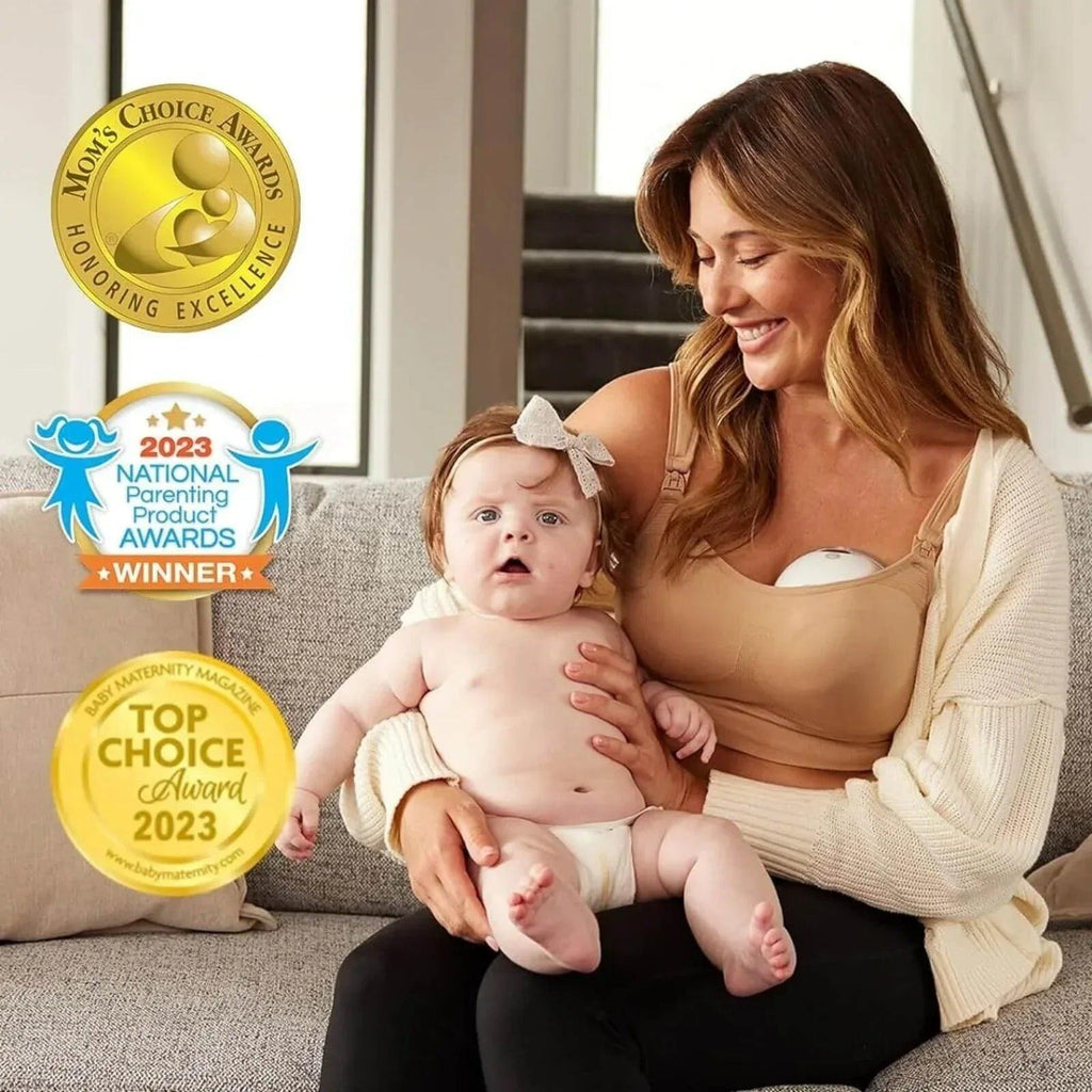 Mother holding baby while wearing a beige wearable breast pump