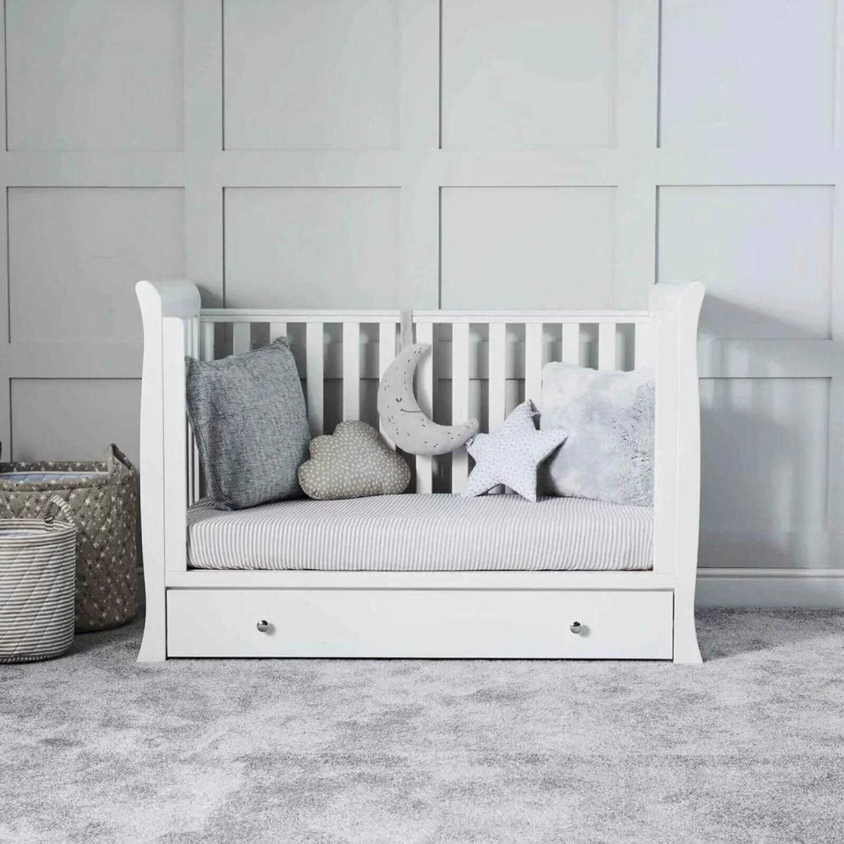 White baby crib with striped mattress and plush star and moon toys