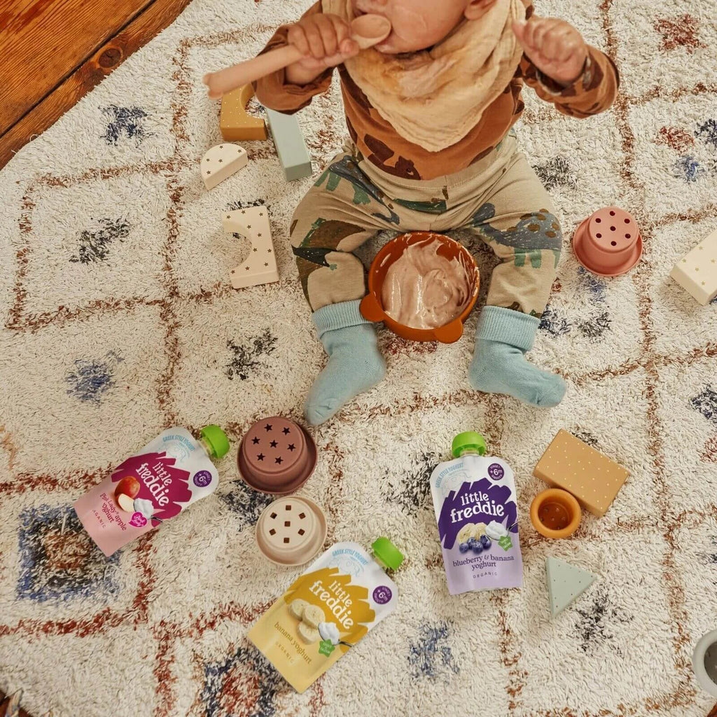 Multiple Little Freddie yogurt pouches scattered on play rug