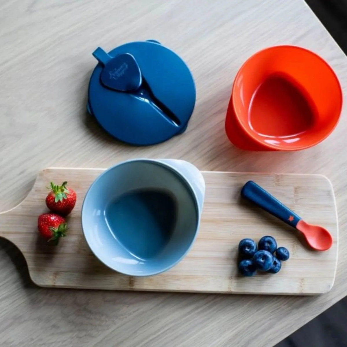 Two baby feeding bowls and spoons on a tray: blue bowl, orange bowl