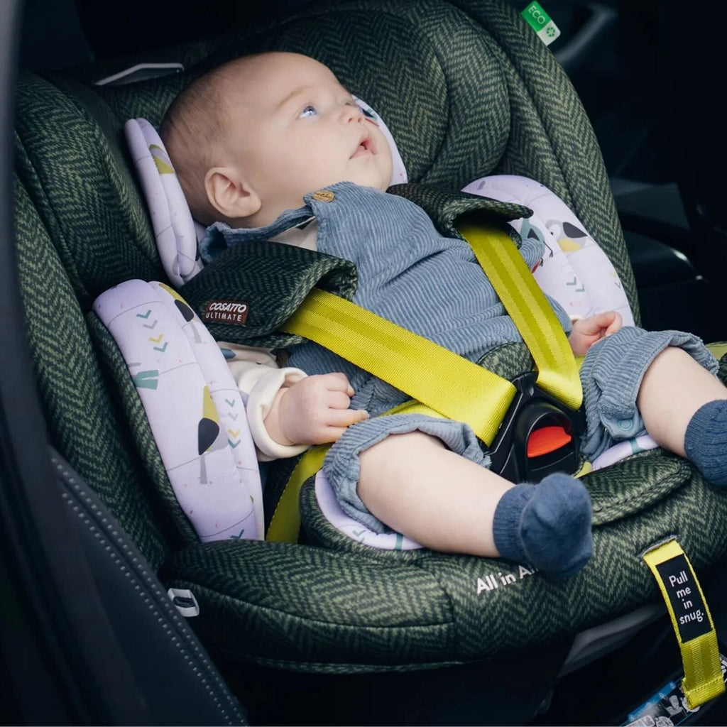 Infant in green Cosatto car seat with patterned inserts, harness straps and yellow belt