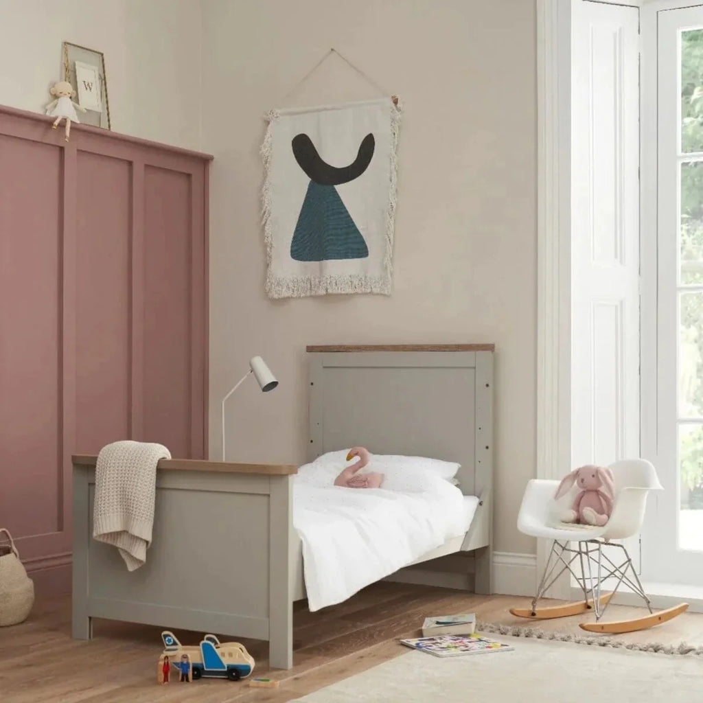 White and dove grey cot bed with oak-toned top rail and open front, shown with bedding