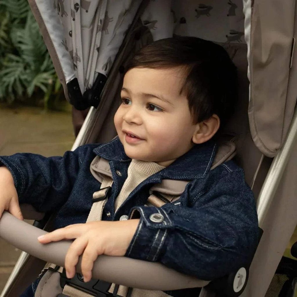 Lightweight stroller with seated child, denim jacket, front view on beige seat