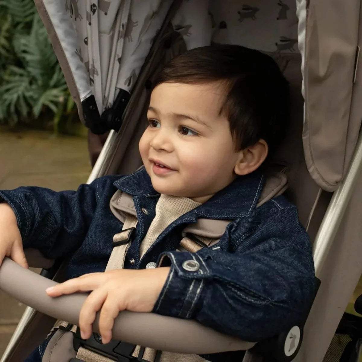 Lightweight stroller with seated child, denim jacket, front view on beige seat