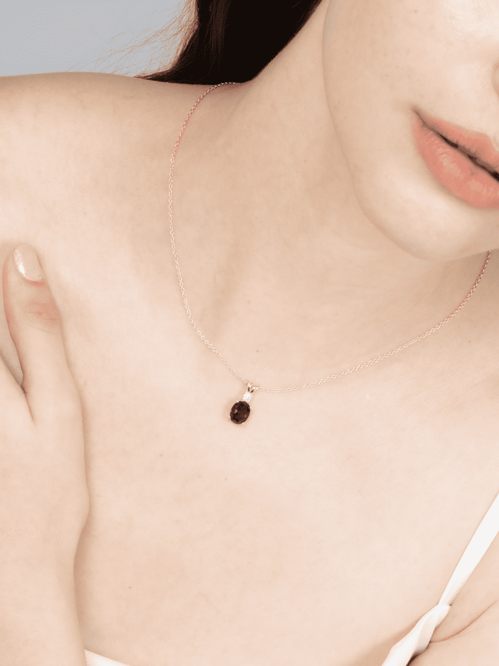 Thin chain necklace with small red bezel charm near collarbone