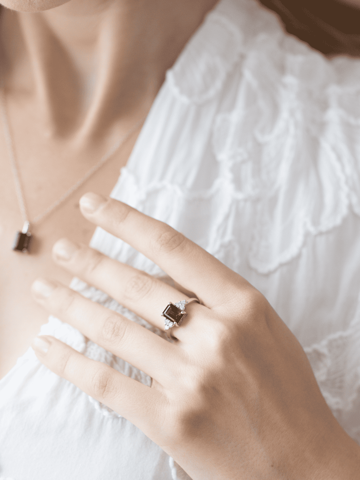 Silver ring with red square gemstone on hand, over white lace fabric
