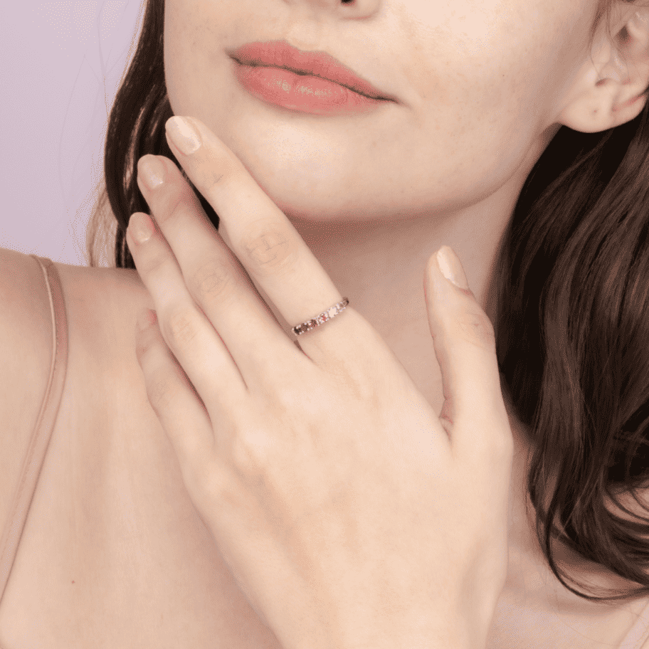Pink gemstone eternity ring on finger with a slim band of alternating stones