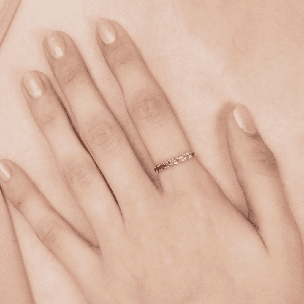 Pink gemstone eternity ring on open palm, showing a slim row of stones