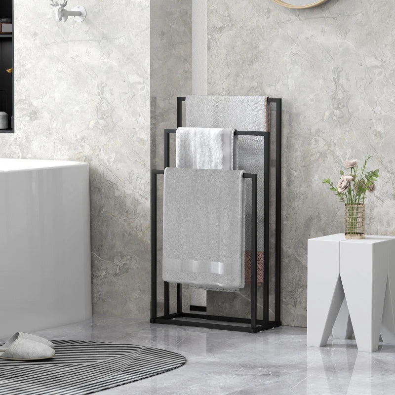 Black freestanding towel rack with three bars, holding gray towels in a bathroom.
