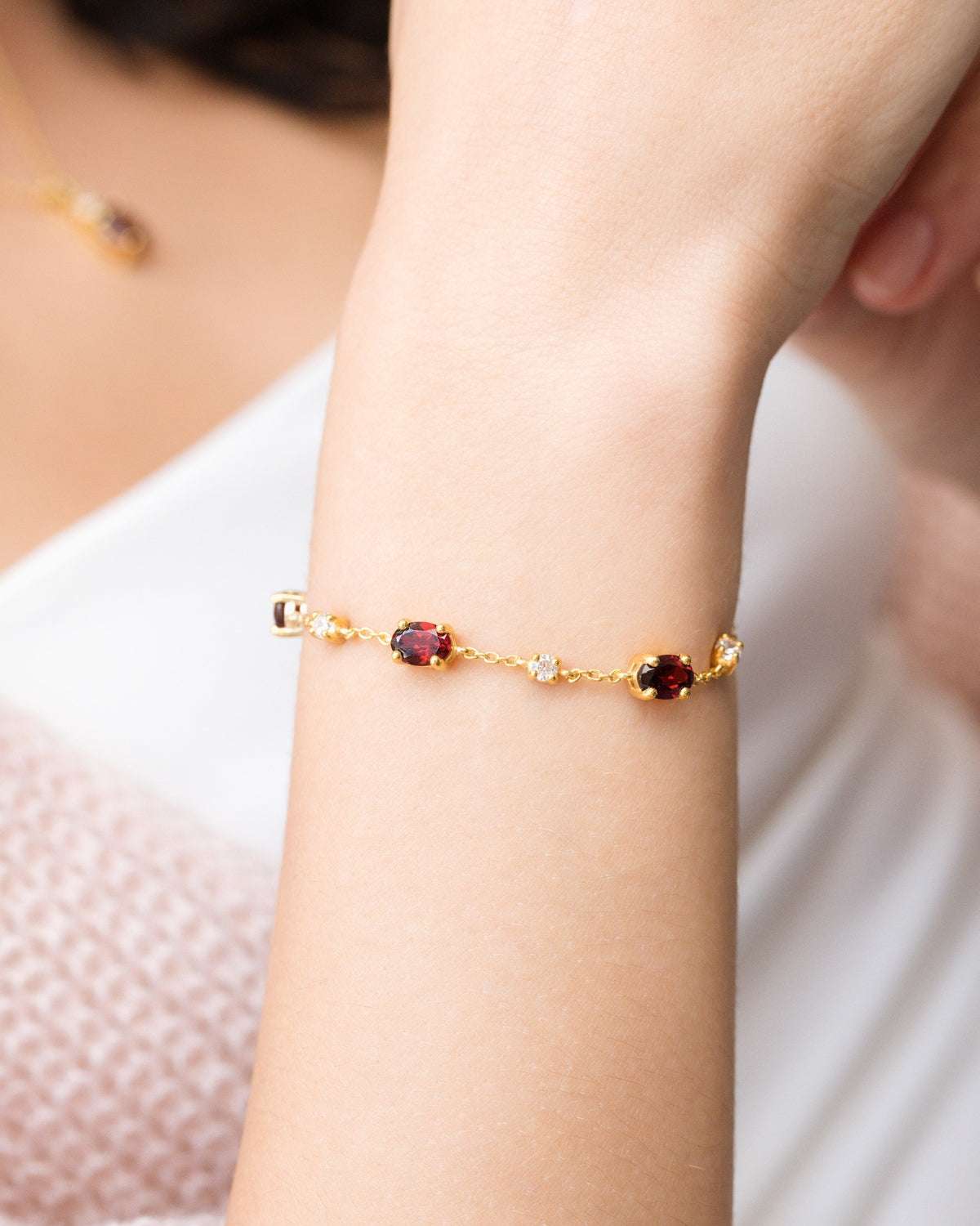 Bracelet close-up with gold chain and garnet oval stones spaced along the band