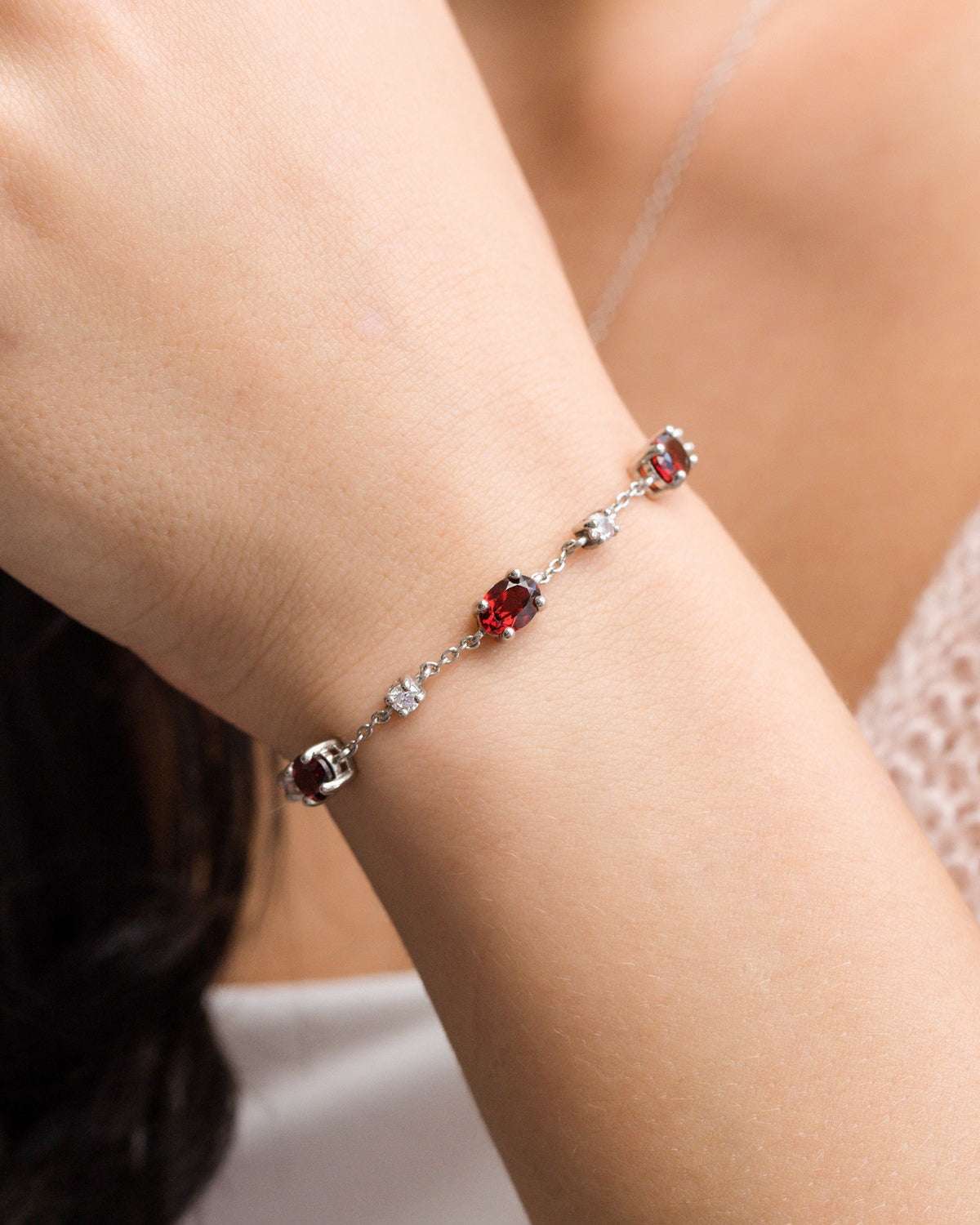 Sterling silver bracelet with red gemstone stations and clear accent stones on wrist