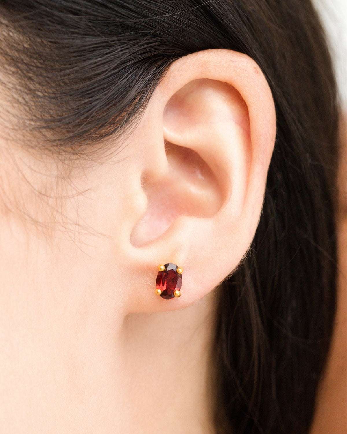 Small red oval garnet stud earrings in gold-toned setting